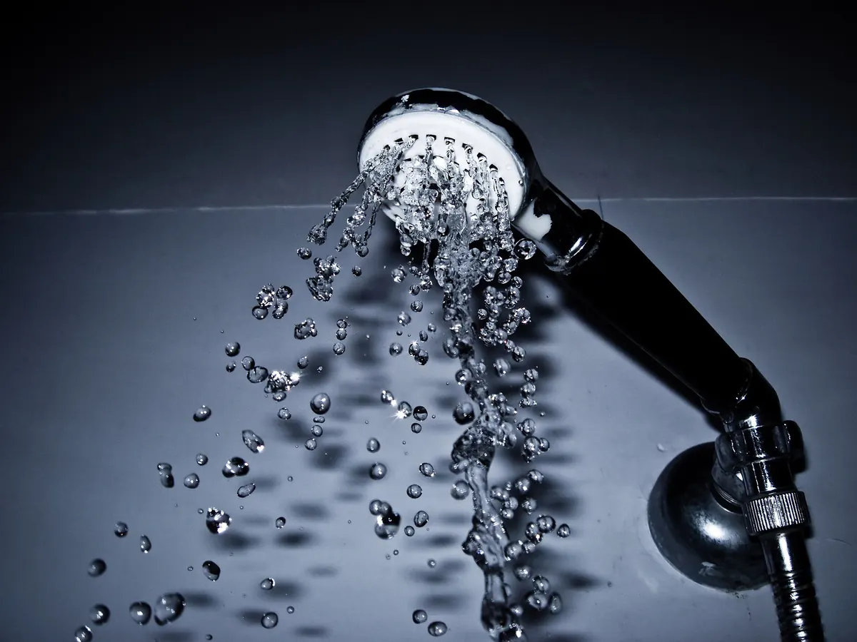 A handheld shower head spraying water against a dark background